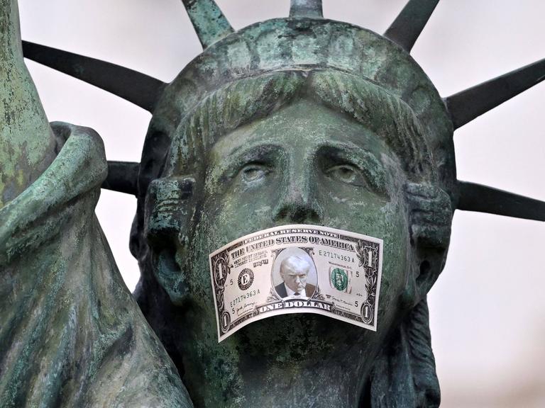 Nachbildung der Freiheitsstatue mit einer Dollarnote als Knebel, die Donald Trumps Porträt zeigt. (Aktion des Künstlers Toolate in Nizza)