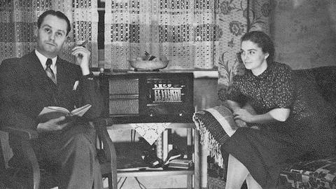 Ein gut bürgerliches Ehepaar sitzt in ihrer Wohnung an einem Volksempfänger.