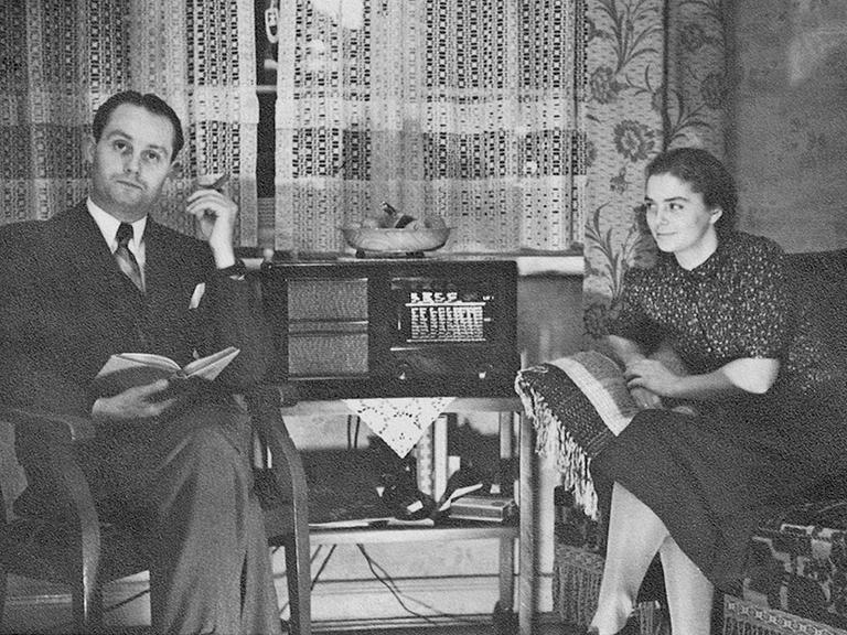 Ein gut bürgerliches Ehepaar sitzt in ihrer Wohnung an einem Volksempfänger.