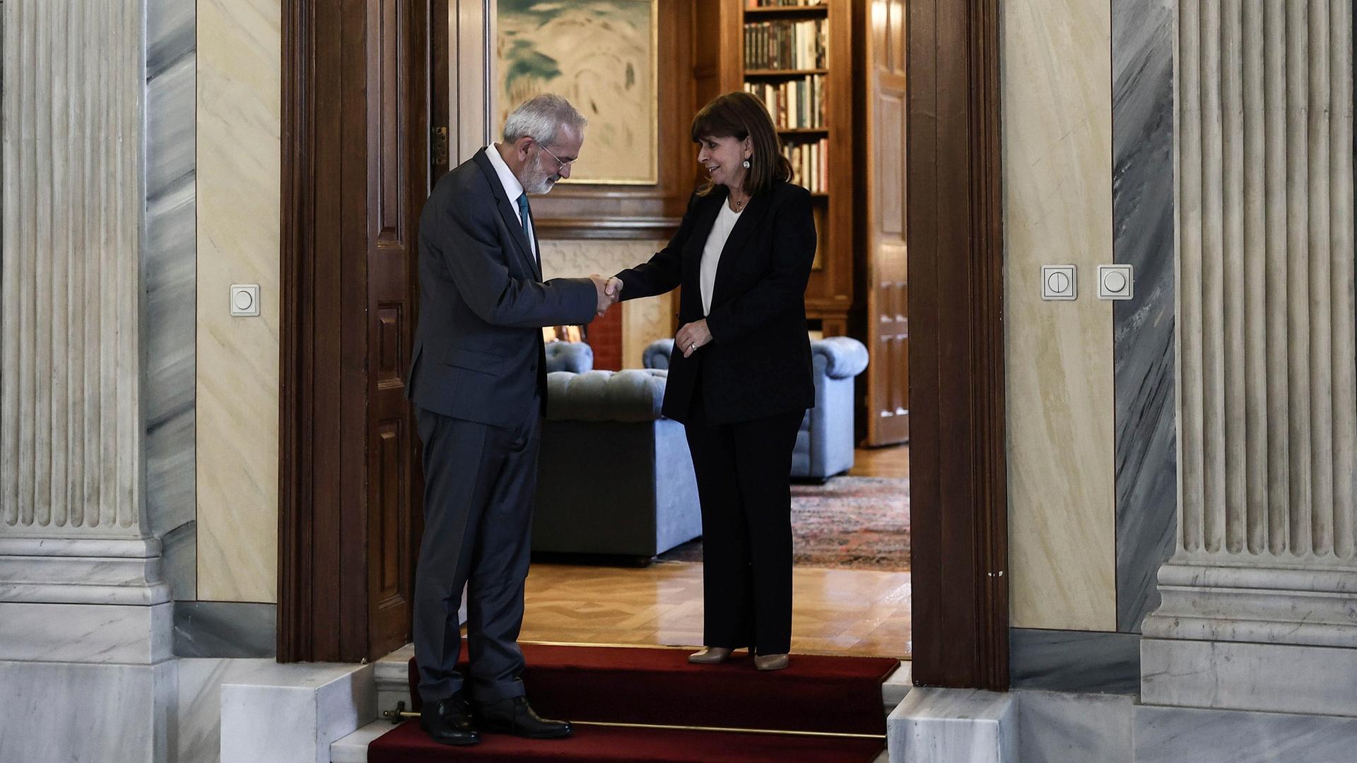 Die griechische Präsidentin Sakellaropoulou und der bisherige Präsidenten des Rechnungshofes und neuer Interimsregierungschef, Sarmas, stehen in der Tür eines Zimmers und schütteln sich die Hände.