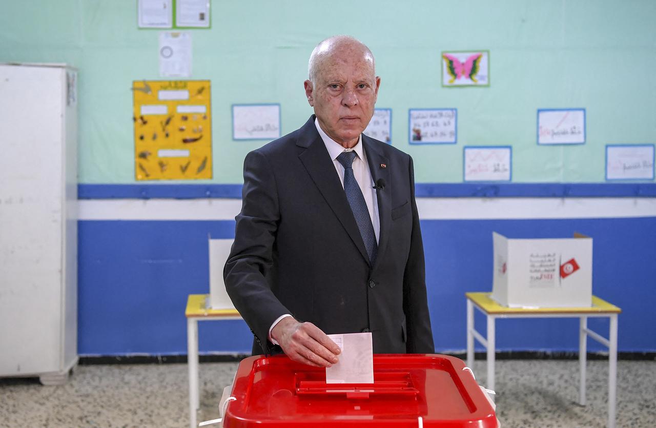 Kais Saied wirft während der Parlamentswahl 2022 seinen Stimmzettel in eine Wahlurne. Er trägt einen schwarzen Anzug und schaut ernst in die Kamera.
