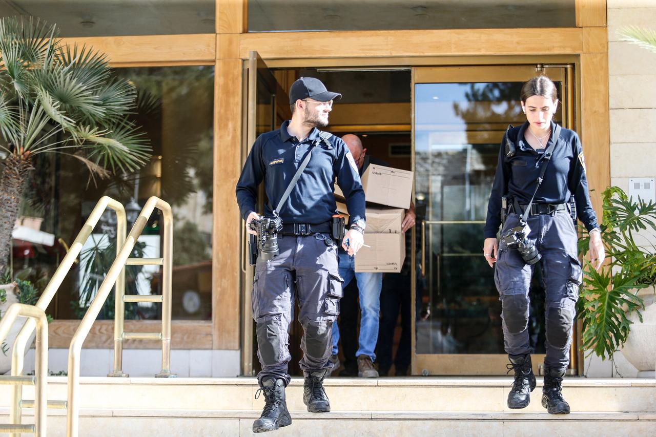Zwei Polizisten laufen aus dem Gebäude von Al Jazeera in Jerusalem. Im Hintergrund trägt ein Mann Kartons hinaus.