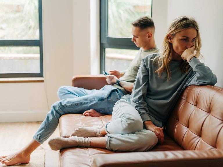 Ein Mann und eine Frau sitzen auf eine Couch. Sie hat ihm den Rücken zugewendet.