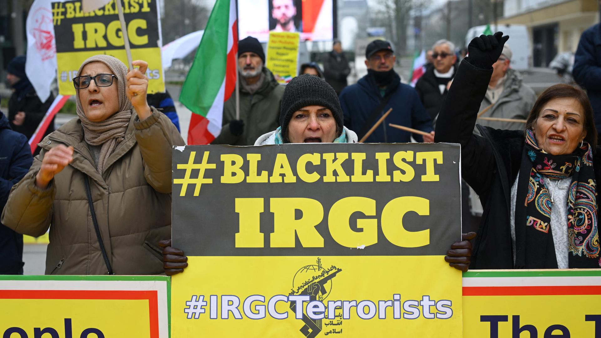 Das Bild zeigt demonstrierende Menschen auf einer Straße in Brüssel. Sie halten gelbe Schilder mit dem Aufdruck "#BLACKLIST IRGC" und fordern damit die Einstufung der iranischen Revolutionsgarde als Terrororganisation.