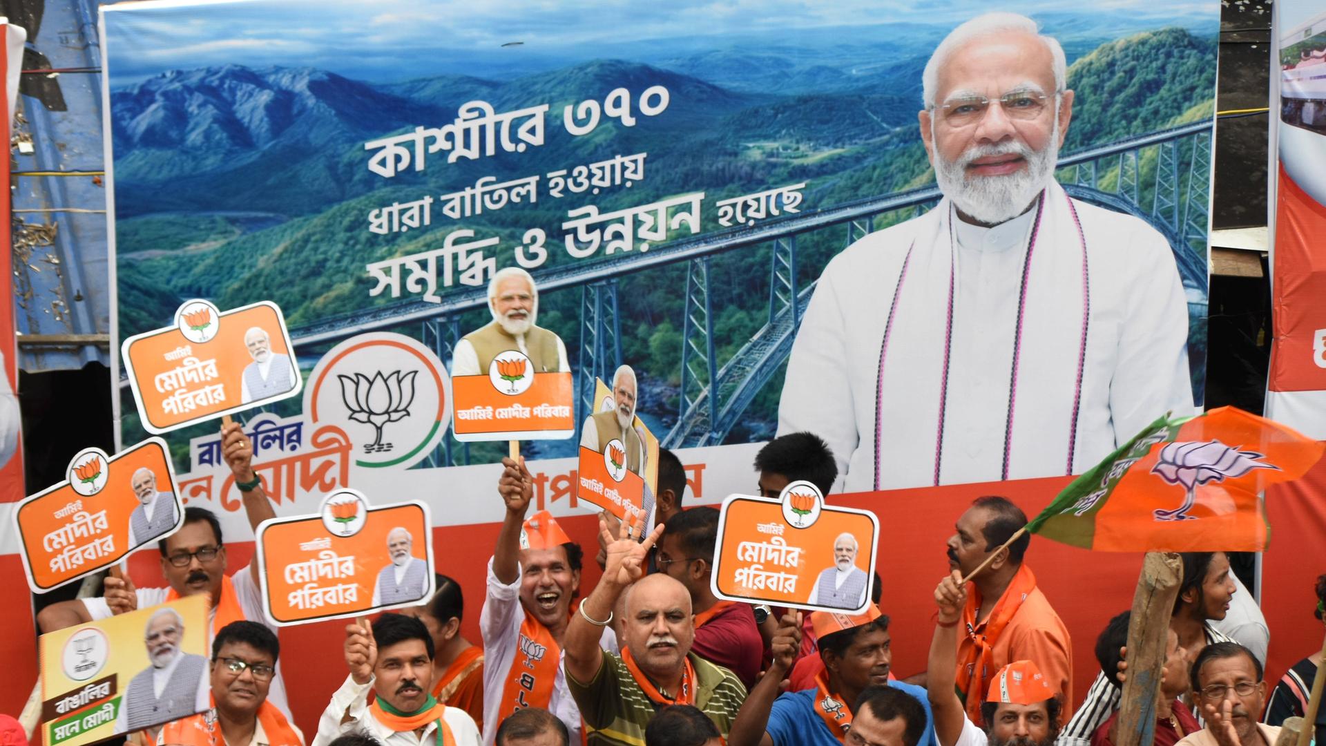 Anhänger von Indiens Premierminister Modi laufen an einem großen Plakat des Politikers vorbei. Sie tragen Schilder mit Wahlslogans. Anhänger von Indiens Premierminister Modi laufen an einem großen Plakat des Politikers vorbei. Sie tragen Schilder mit Wahlslogans.