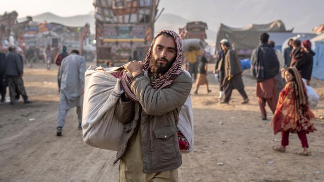Ein Mann mit Bart trägt eine große Tasche über der Schulter. Er geht über eine staubige Straße. Es ist ein Mann aus Afghanistan. Das Bild ist von der Grenze zwischen Afghanistan und Pakistan.