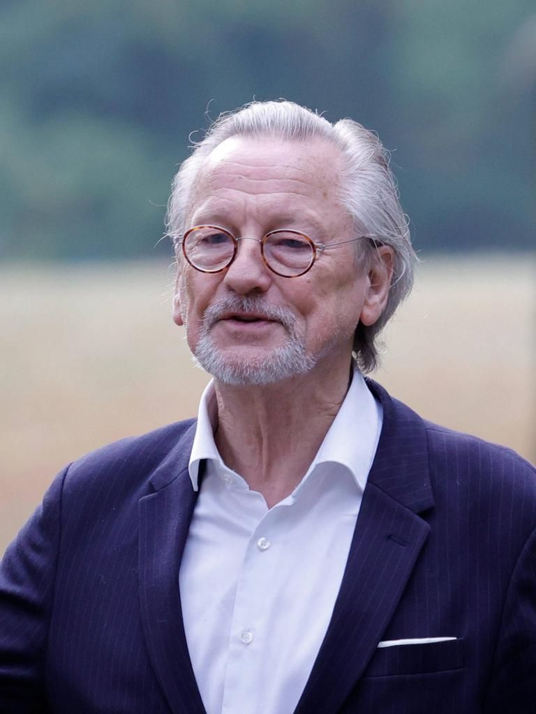 Peter Brandt trägt Anzug und ein weißes Hemd und steht gestikulierend auf einer Wiese.