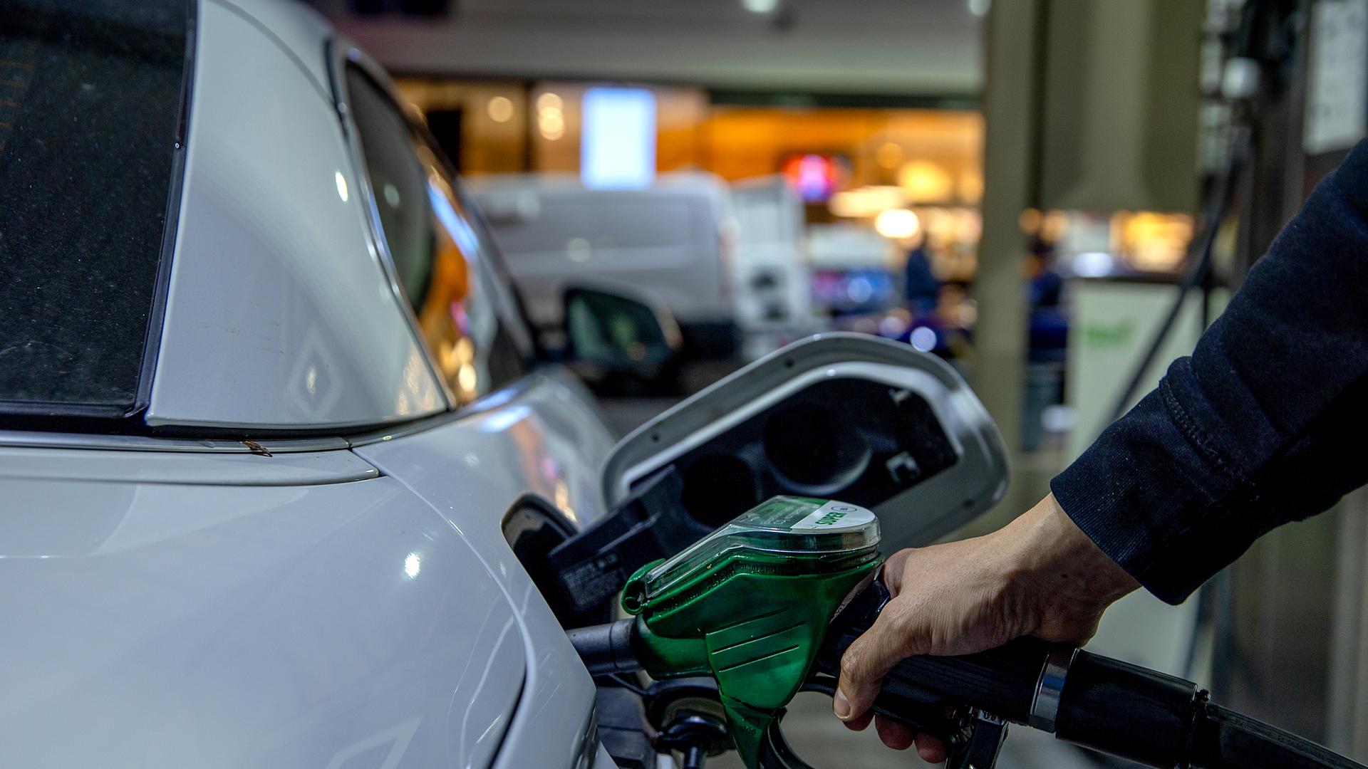 Das Bild zeigt einen Menschen, der an der Tankstelle sein Auto mit Kraftstoff füllt.