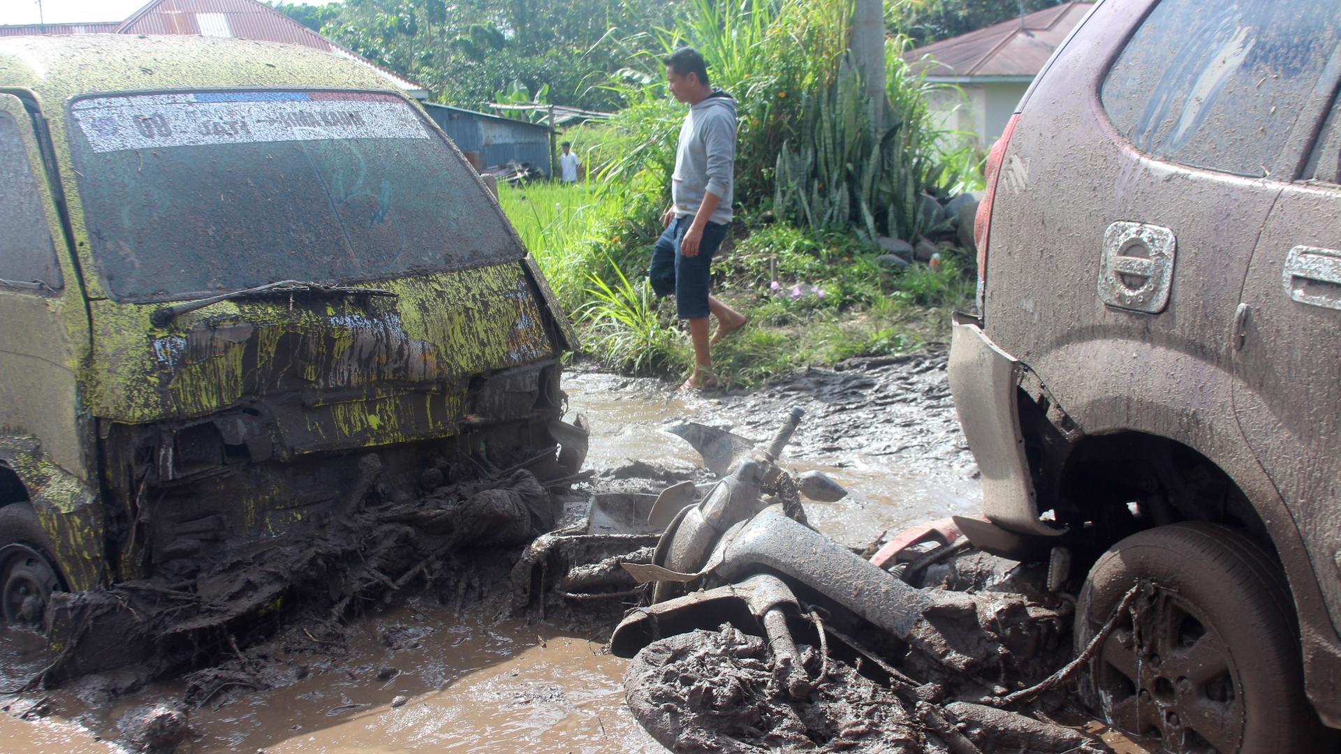Indonesien, Agam: Ein Mann geht an den Wracks von Autos und einem Motorrad vorbei, die von einer Sturzflut weggeschwemmt wurden. Indonesien, Agam: Ein Mann geht an den Wracks von Autos und einem Motorrad vorbei, die von einer Sturzflut weggeschwemmt wurden.
