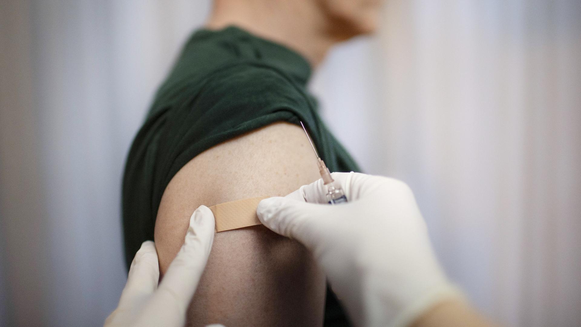 Impfung. Ein Arzt klebt ein Pflaster auf die Einstichstelle am Arm.