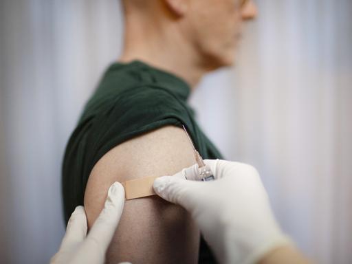 Impfung. Ein Arzt klebt ein Pflaster auf die Einstichstelle am Arm.