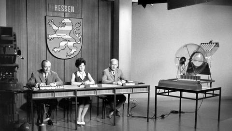 Aufnahme aus der Zeit der Anfänge der Ziehung der Lottozahlen im Studio des Hessischen Rundfunks in Frankfurt am Main, v.l.: Regierungsdirektor H.-R. Bode als Aufsichtsbeamter, Ziehungsassistentin Luise Roth und Ziehungsleiter Helmut Hübner.