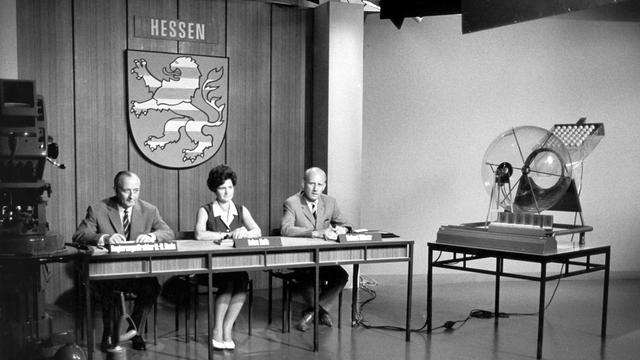 Aufnahme aus der Zeit der Anfänge der Ziehung der Lottozahlen im Studio des Hessischen Rundfunks in Frankfurt am Main, v.l.: Regierungsdirektor H.-R. Bode als Aufsichtsbeamter, Ziehungsassistentin Luise Roth und Ziehungsleiter Helmut Hübner.