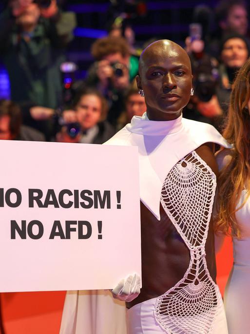 Model Papis Loveday, der ein Schild mit den Worten No Racism, No AfD hochhält,  und Schauspielerin Pheline Roggan, die eine Kette mit den Buchstaben FCK AFD trägt, bei der Festivaleröffnung der Berlinale.
