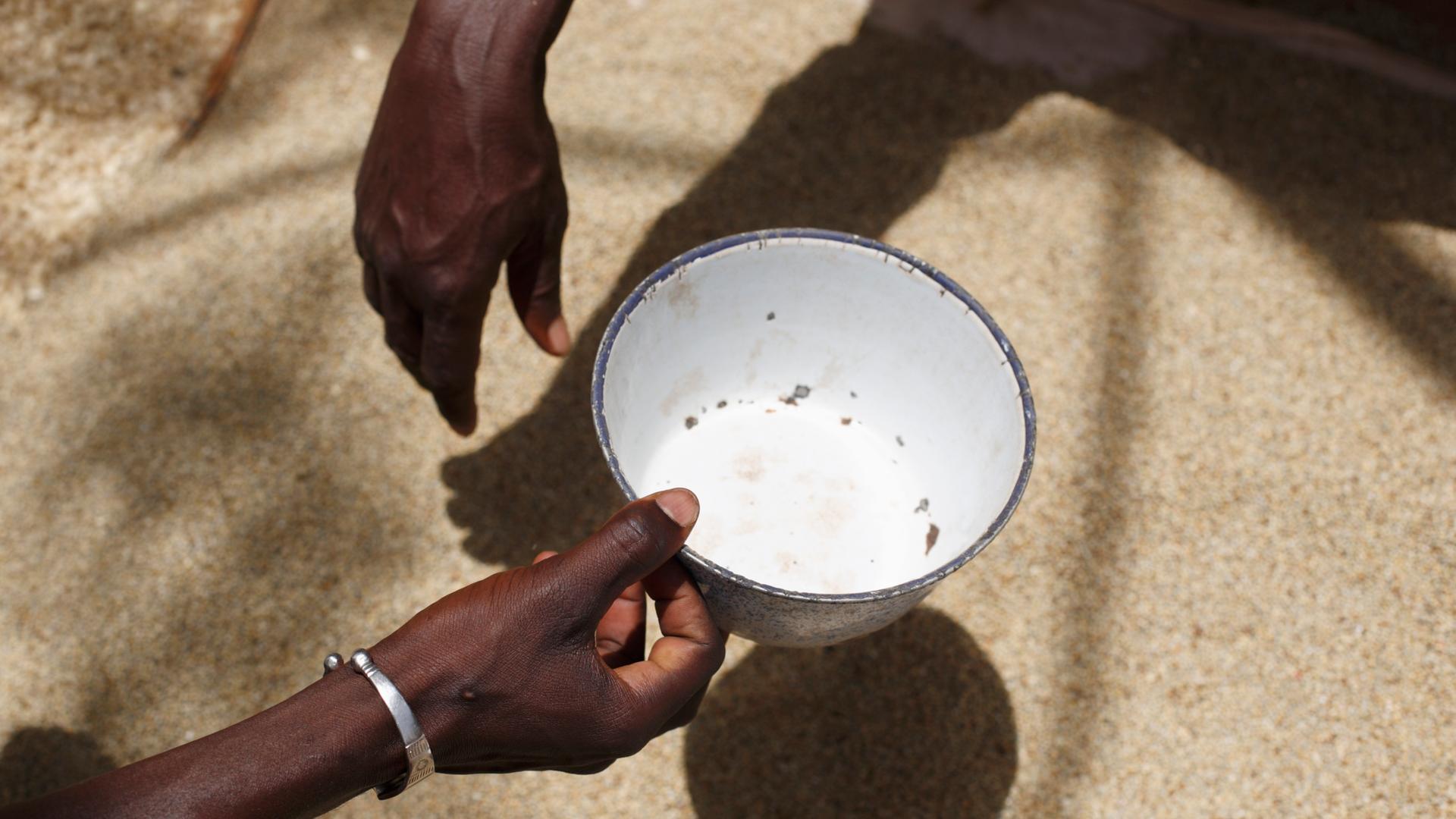 Auf einem Markt in Ouagadougou, in Burkina Faso, hält eine Frau eine leere Emailleschüssel über einen Sack mit Reis.