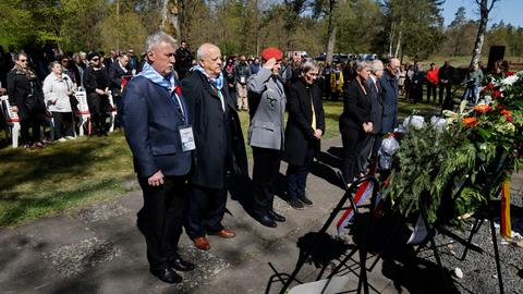 Menschen stehen vor Blumenkränzen während einer Trauerzeremonie auf dem Friedhof für Kriegsgefangene in Lohheide.