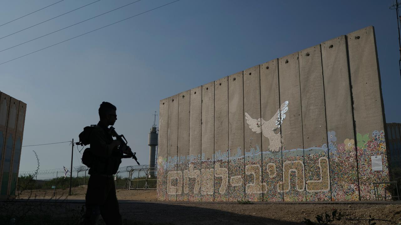 Im Kibbutz Netiv Haasara nahe der Grenze zum Gazastreifen steht ein israelischer Soldat. Im Hintergrund steht eine Sicherheitsmauer mit einer Friedenstaube darauf.