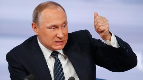 Porträt von Wladimir Putin vor zwei Mikrofonen. Er guckt böse, während er spricht und hat die Faust erhoben, als wolle er damit auf den Tisch hauen.