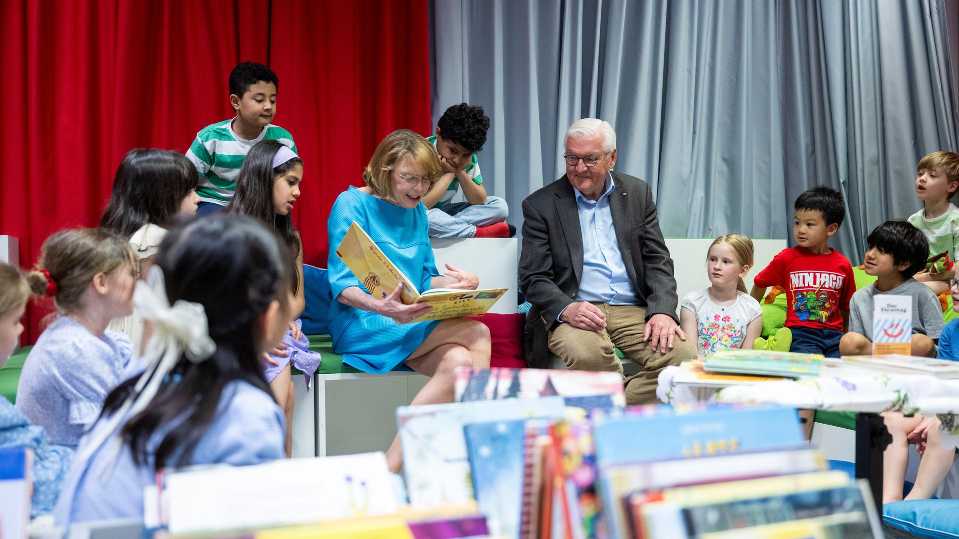 Der Bundes-Präsident sitzt neben seiner Frau. Die Frau hat ein Buch auf dem Schoß und liest daraus vor. Neben den beiden sind viele kleine Kinder. Die Kinder hören gespannt zu. Der Bundes-Präsident sitzt neben seiner Frau. Die Frau hat ein Buch auf dem Schoß und liest daraus vor. Neben den beiden sind viele kleine Kinder. Die Kinder hören gespannt zu.