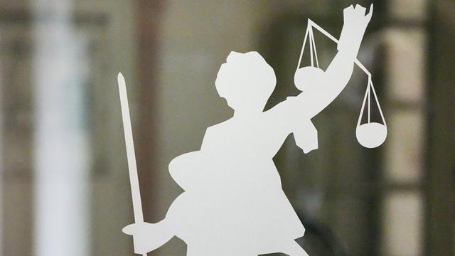 Silhouette der Justitia mit Richtschwert und Waage auf dem Glasfenster einer Tür im Gerichtsgebäude