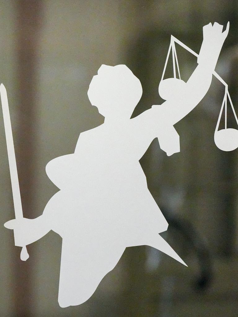 Silhouette der Justitia mit Richtschwert und Waage auf dem Glasfenster einer Tür im Gerichtsgebäude