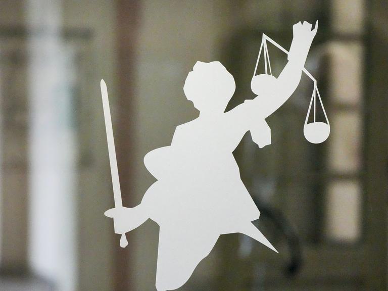 Silhouette der Justitia mit Richtschwert und Waage auf dem Glasfenster einer Tür im Gerichtsgebäude