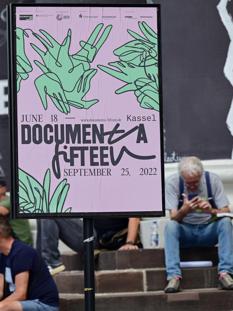 Besucher der documenta fifteen sitzen auf den Stufen des Fridericianums vor bemalten Säulen des Gebäudes; rechts ein Plakat der documenta
