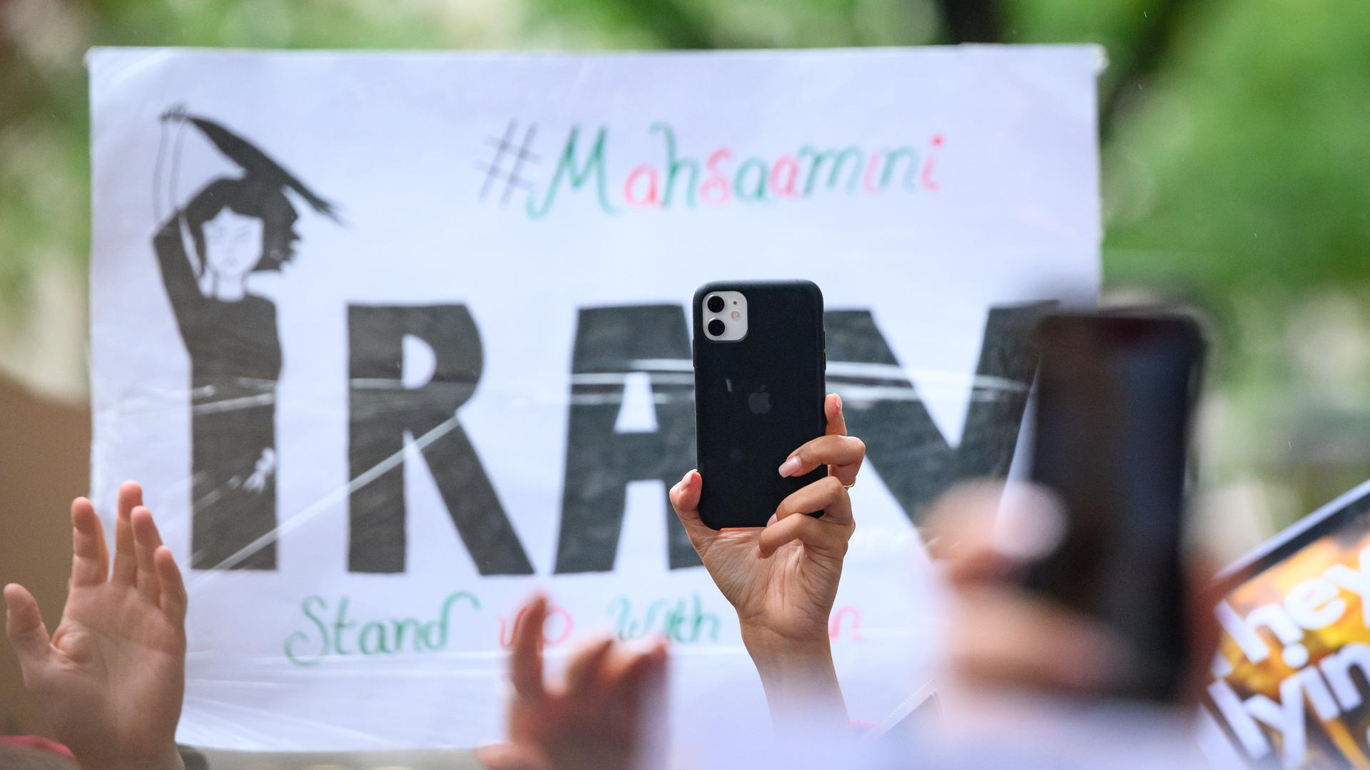 Ein Smartphone wird vor einem Plakat in die Höhe gehalten auf einer Solidaritätskundgebung nach dem Tod der Iranerin Mahsa Amini, die in Iran in Polizeigewahrsam gestorben war.