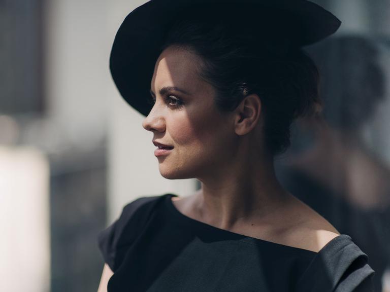 Katharina Konradi mit dunklem Hut steht zwischen Licht und Schatten. Ihr Gesicht ist im Profil zu sehen.