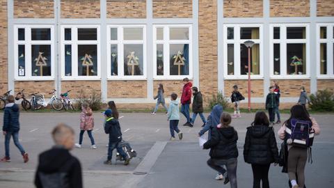 Mehrere Schüler laufen über einen Pausenhof zum Schulgebäude.