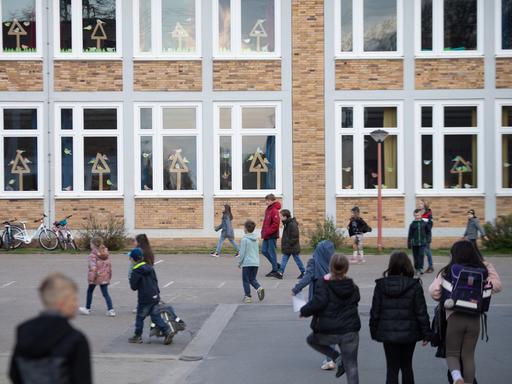 Mehrere Schüler laufen über einen Pausenhof zum Schulgebäude.