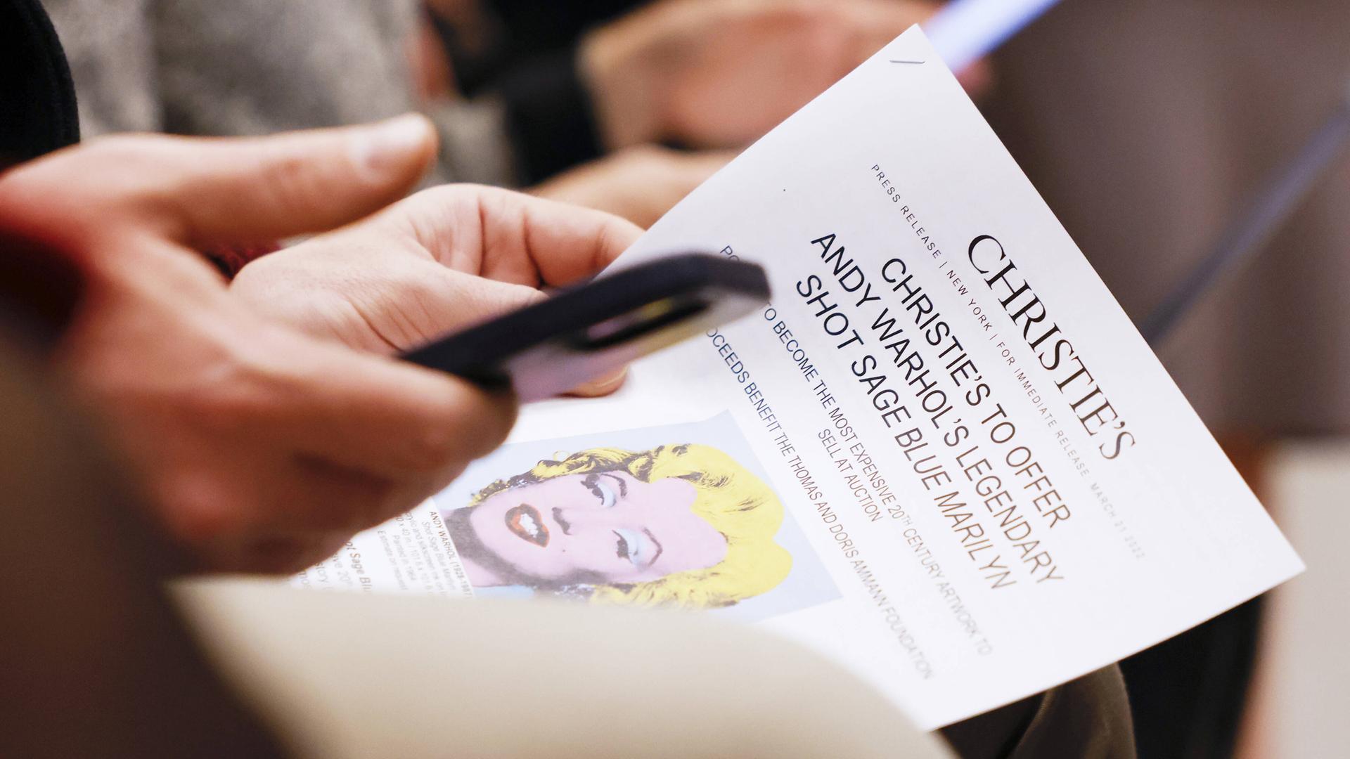 Eine Pressemitteilung darüber, dass das Bild "Shot Sage Blue Marilyn" von Andy Warhol beim Auktionshaus Christie's versteigert wird, wird in der Hand gehalten. Eine Pressemitteilung darüber, dass das Bild "Shot Sage Blue Marilyn" von Andy Warhol beim Auktionshaus Christie's versteigert wird, wird in der Hand gehalten.