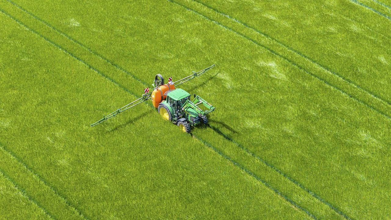 Das Drohnenfoto zeigt einen Traktor, der über eine Sprühvorrichtung mit zwei seitlichen Auslegern Flüssigkeit aus einem Tank auf einem Feld verteilt.