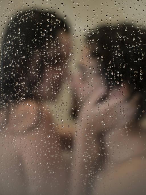 Junges Paar tauscht Zärtlichkeiten unter der Dusche aus.