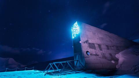 Aufragender Eingang zu einem unteridisch liegenden Gebäude mit der Aufschrift "Global Seed Vault". Seine Beleuchtung hebt es vor dem Sternenhimmel ab.