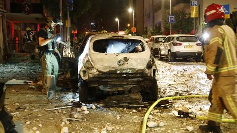 Feuerwehrleute in Tel Aviv untersuchen ein zerstörtes Auto nach einem Hamas-Raketenangriff in der Innenstadt.