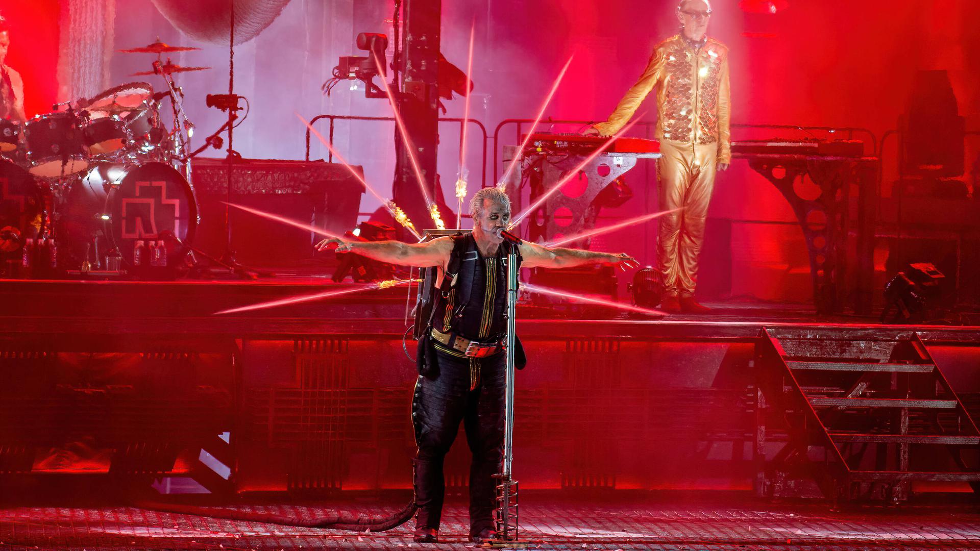 Die Band Rammstein mit Frontmann Till Lindemann, der ein Feuerwerk spuckendes Jetpack auf dem Rücken trägt, in roten Licht getaucht bei einem Konzert in Aarhus, Dänemark