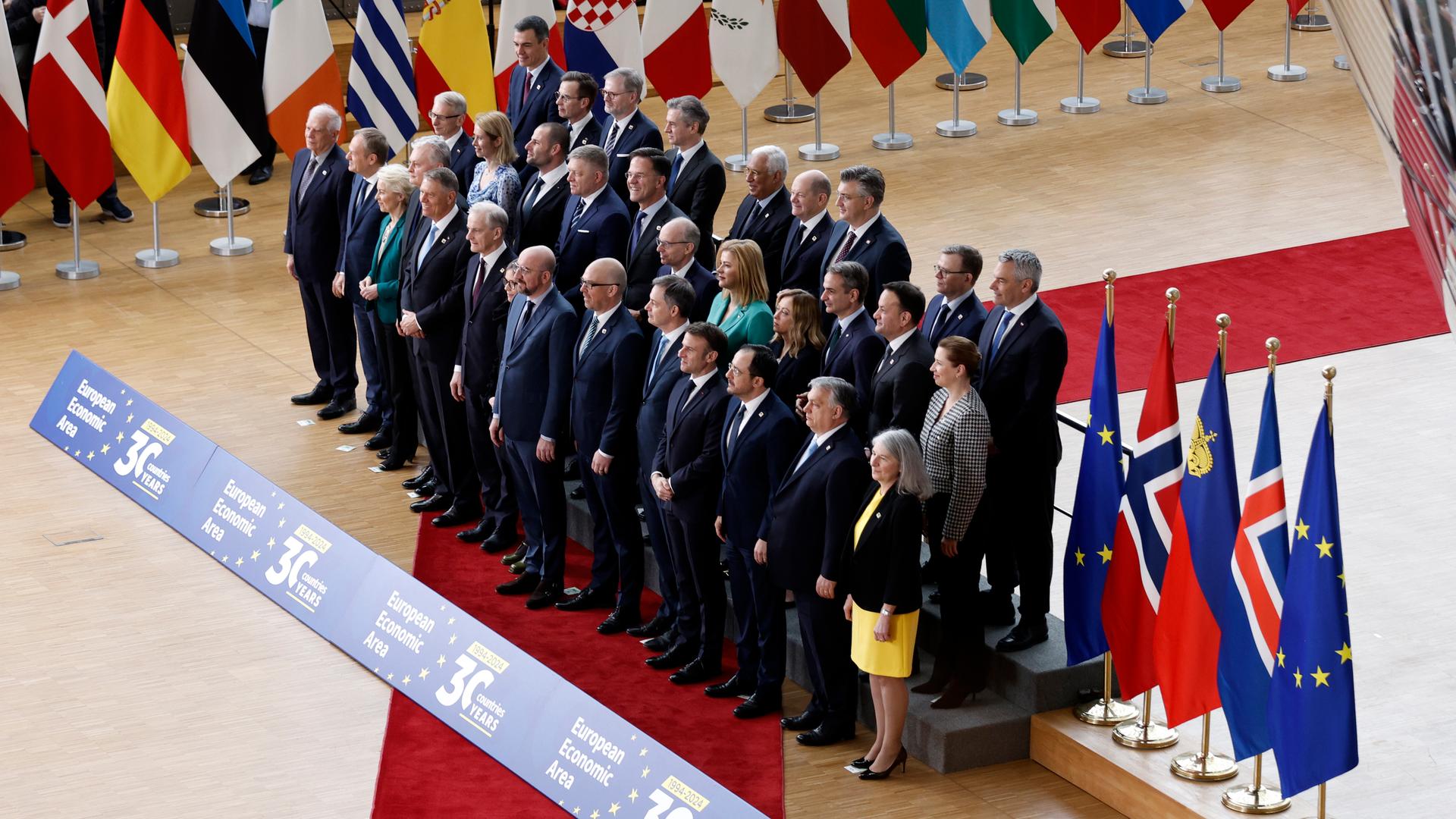 Die Staats- und Regierungschefs stehen für ein Foto zusammen. Um sie herum stehen die Landesfahnen.