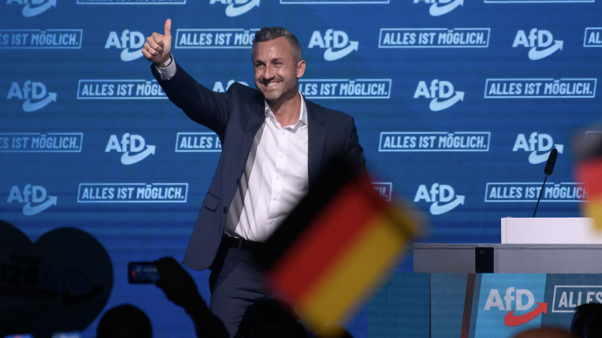 Siegmund steht auf einer Bühne und reckt einen Daumen nach oben. Vor ihm stehen Anhänger, hinter ihm ist mehrere Male das Parteilogo an der Wand zu sehen. Siegmund steht auf einer Bühne und reckt einen Daumen nach oben. Vor ihm stehen Anhänger, hinter ihm ist mehrere Male das Parteilogo an der Wand zu sehen.