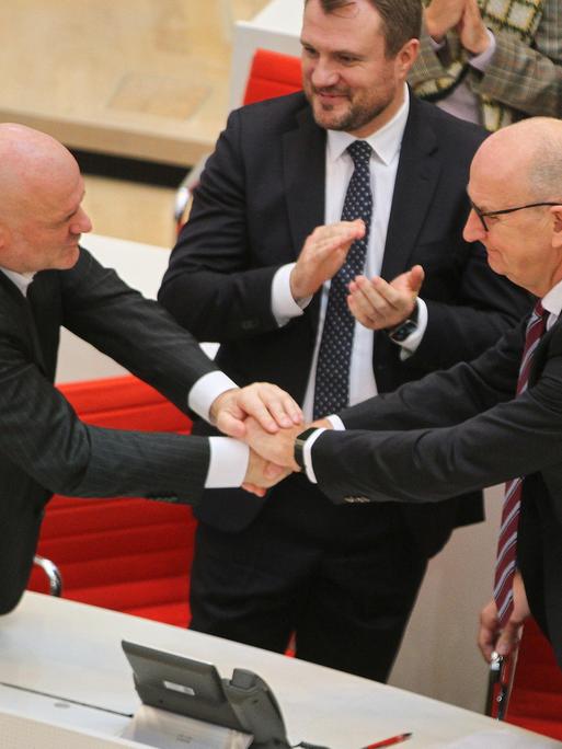 Robert Crumbach und Dietmar Woidke gratulieren einander und schütteln sich über einen Tisch hinweg beide Hände.