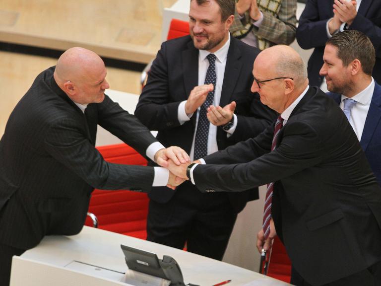 Robert Crumbach und Dietmar Woidke gratulieren einander und schütteln sich über einen Tisch hinweg beide Hände.