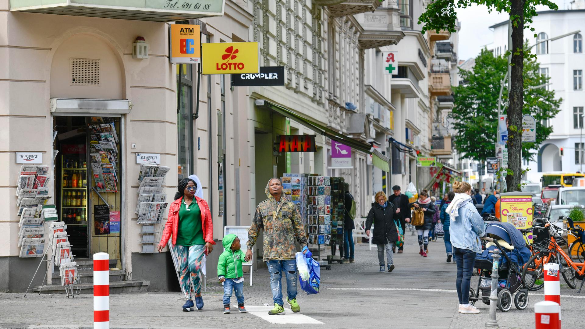 Eine Straßenszene in Berlin-Kreuzberg: Zwei dunkelhäutige Erwachsene und ein kleines Kind wollen eine Straße überqueren. Weitere Personen laufen auf dem Gehsteig.