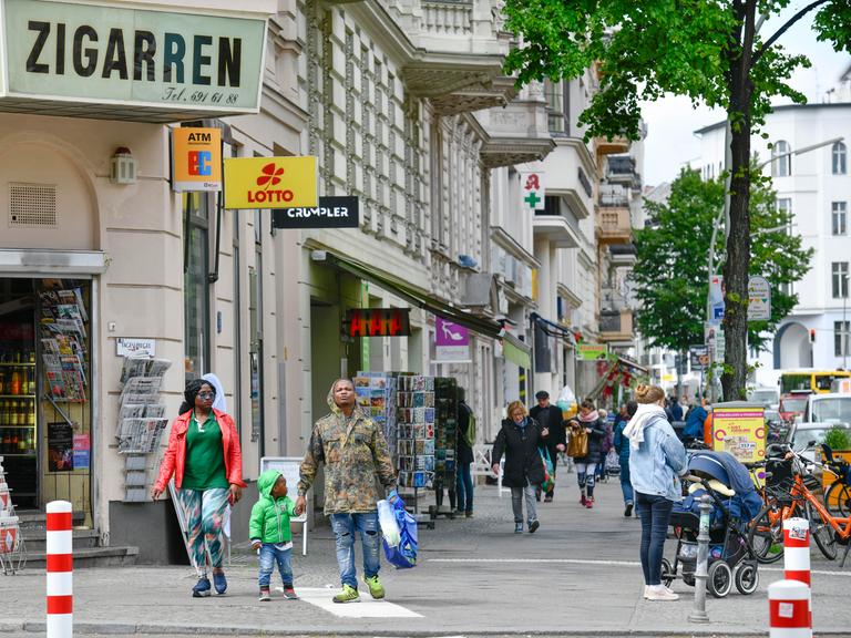 Eine Straßenszene in Berlin-Kreuzberg: Zwei dunkelhäutige Erwachsene und ein kleines Kind wollen eine Straße überqueren. Weitere Personen laufen auf dem Gehsteig.