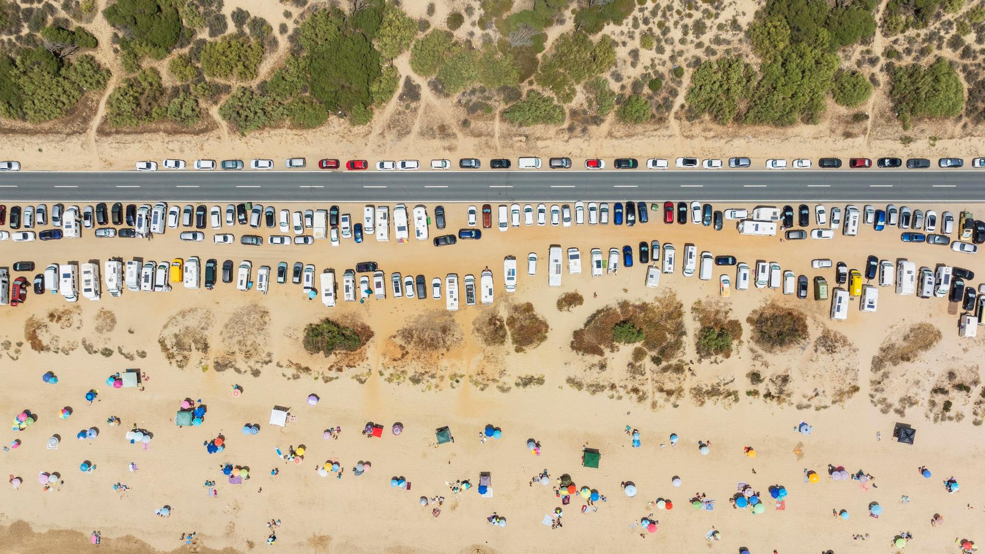 Luftaufnahme eines Strandes in Spanien am Atlantischen Ozean bei Punta Umbria. Der Strand ist voll mit Menschen und an der Strasse reihen sich die geparkten Autos aneinander.