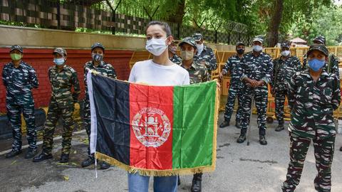 Eine junge Frau, die von indischen Polizistinnen umringt wird, hält eine afghanische Flagge vor sich in die Höhe.