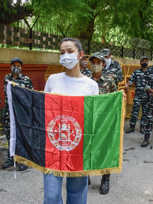 Eine junge Frau, die von indischen Polizistinnen umringt wird, hält eine afghanische Flagge vor sich in die Höhe.