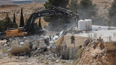 Ein palästinensisches Haus wird von israelischen Siedlern mit einem Bagger zerstört.