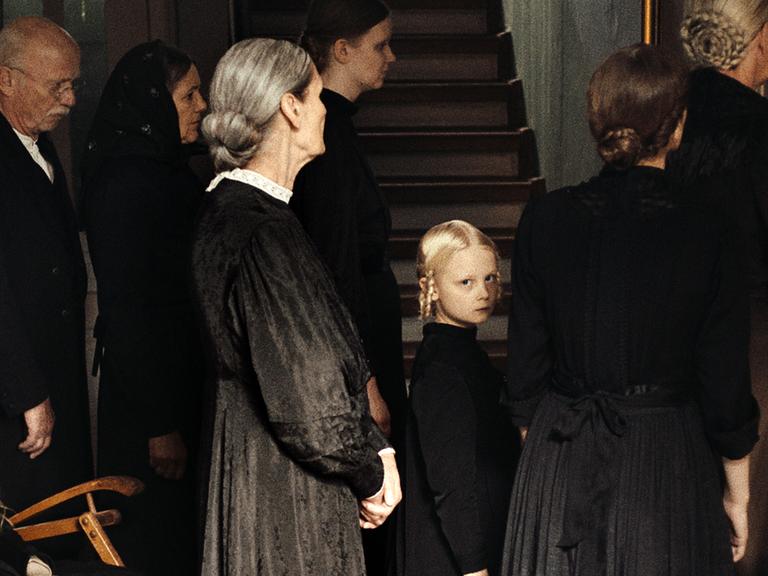 Das Foto zeigt eine Szene aus dem Spielfilm "In die Sonne schauen", in der Alma, gespielt von Hanna Heckt (Mitte), mit ihrer Familie an einer Totenfeier teilnimmt.