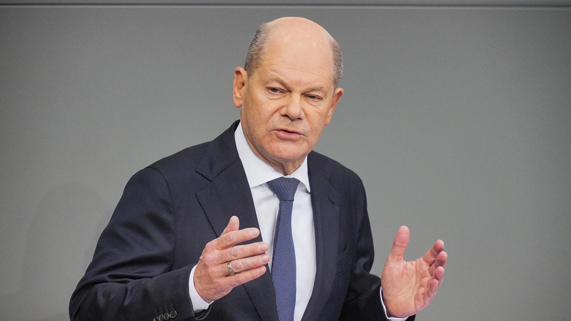 Bundeskanzler Olaf Scholz (SPD) spricht im Bundestag. Er hält die Arme und Hände geöffnet. 