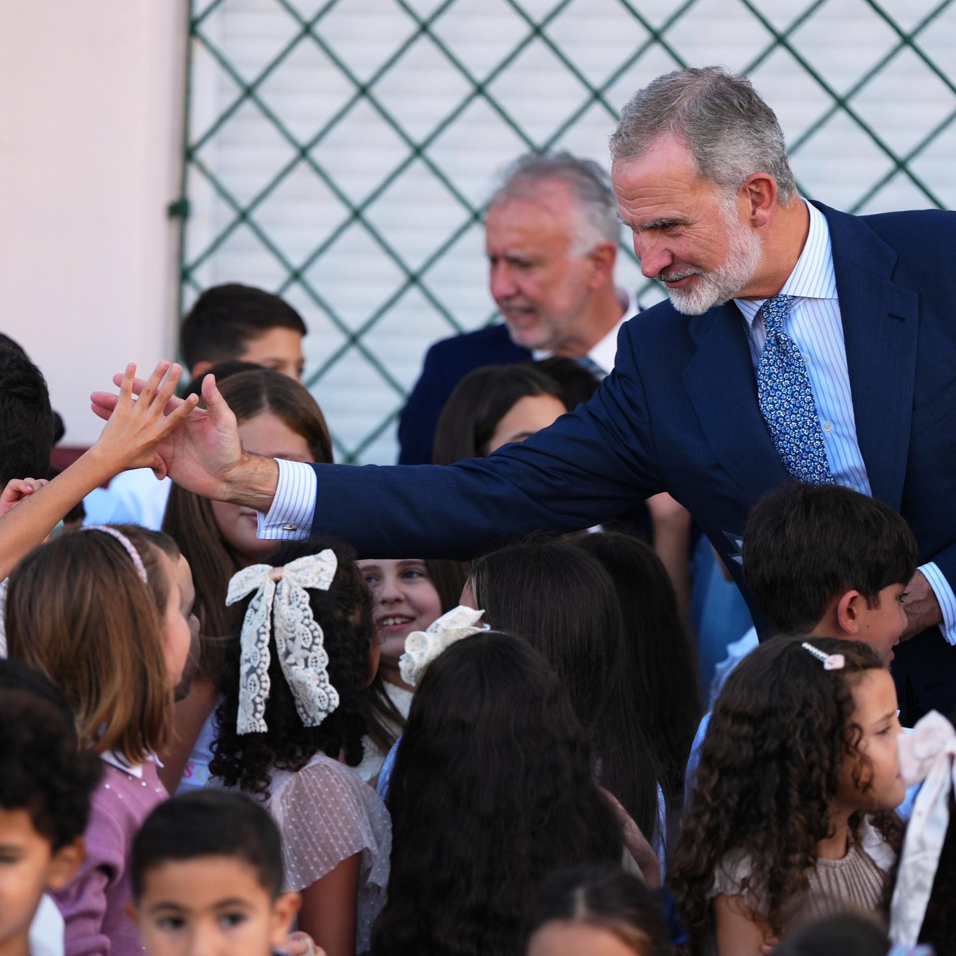 Spaniens König Felipe an einer Schule in Ceuta, inmitten von Kindern. Ein Junge und der König strecken sich die Hand entgegen. 